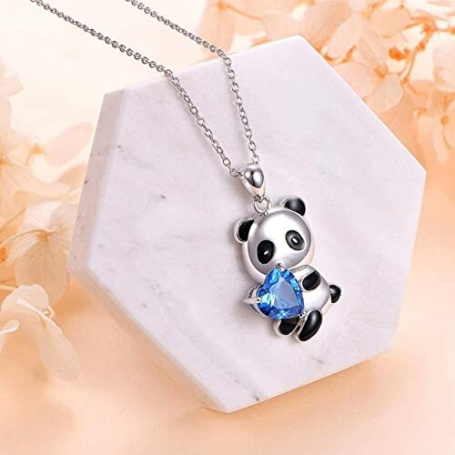 Panda necklace with blue gem on hexagonal marble surface.