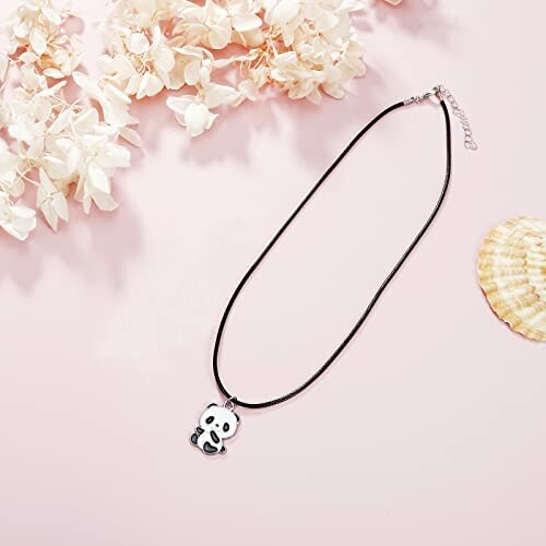 Panda pendant necklace on a pink background with flowers and a shell.