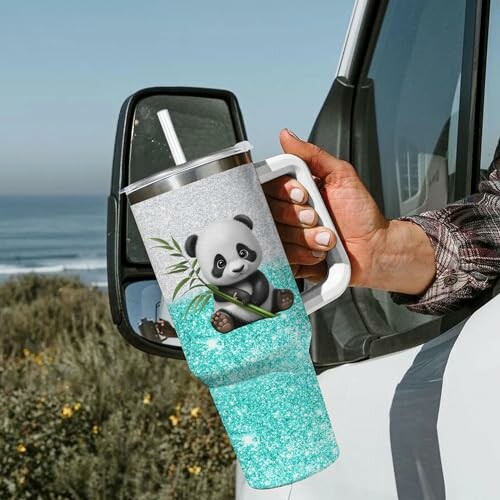 Person holding a large tumbler with a panda design by the seaside.