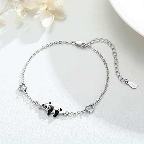 Silver bracelet with panda charm and heart links on a light surface.