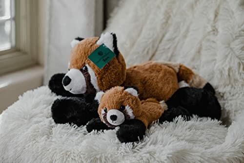 Two stuffed red panda toys on a fluffy white blanket